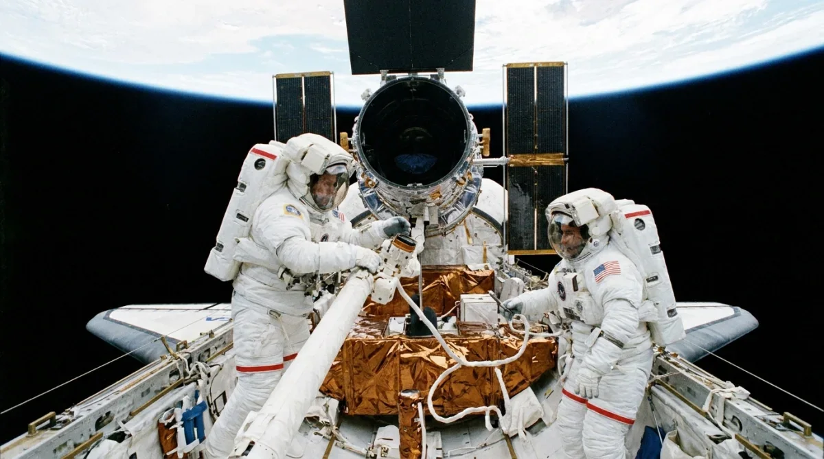 Astronautas realizando caminhada espacial para manutenção dos instrumentos do telescópio Hubble.