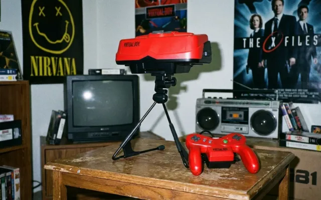 Console Nintendo Virtual Boy apoiado em seu suporte com controle vermelho em uma mesa.