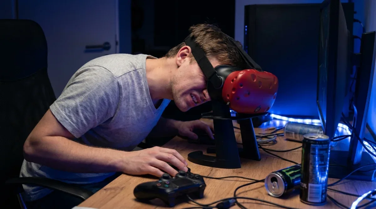 Pessoa curvada sobre uma mesa jogando em um visor de realidade virtual fixo com postura desconfortável.