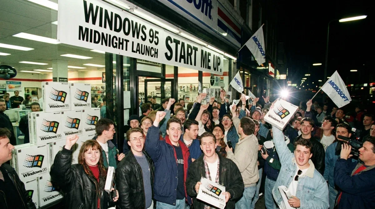 Pessoas reunidas no evento oficial de lançamento do Windows 95 segurando caixas do sistema operacional.