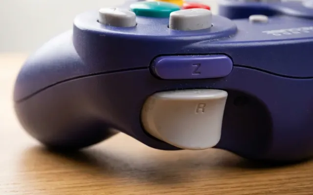 Detalhe do controle de GameCube roxo com foco no botão Z e gatilho superior direito sobre uma mesa de madeira.