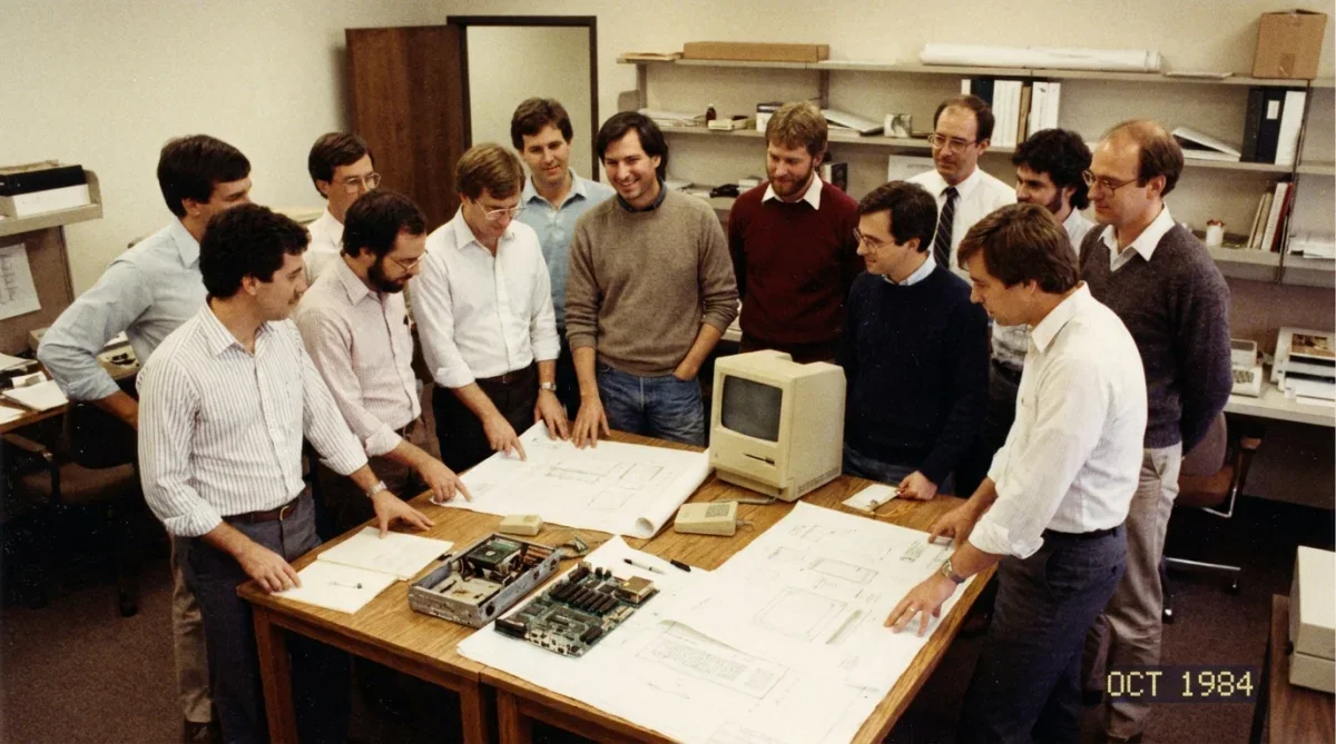 Steve Jobs e a equipe de desenvolvimento do primeiro Macintosh reunidos com protótipos em 1984